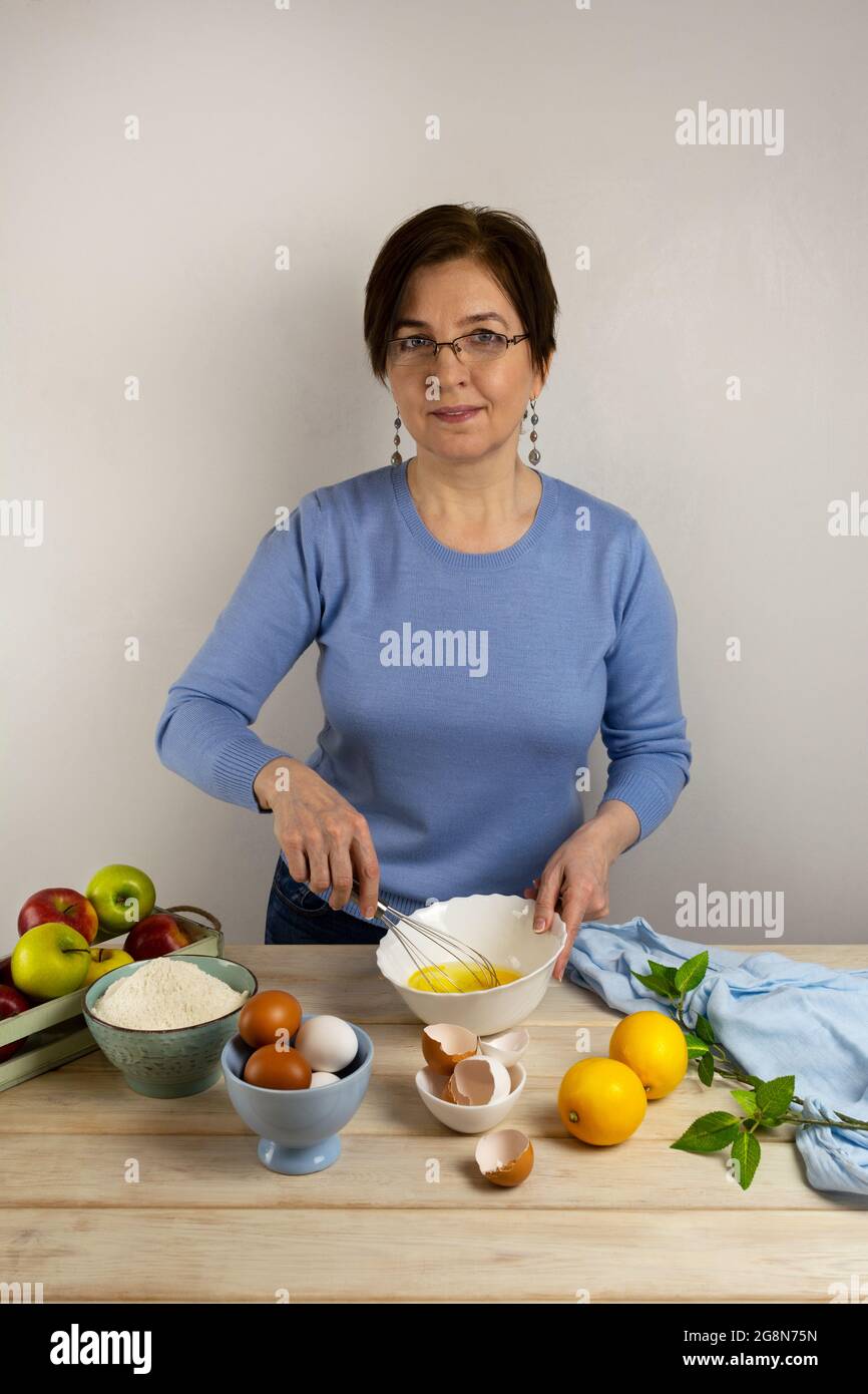 Une femme fouette des œufs avec un fouet dans le bol blanc. Cuisson de la tarte aux pommes Banque D'Images