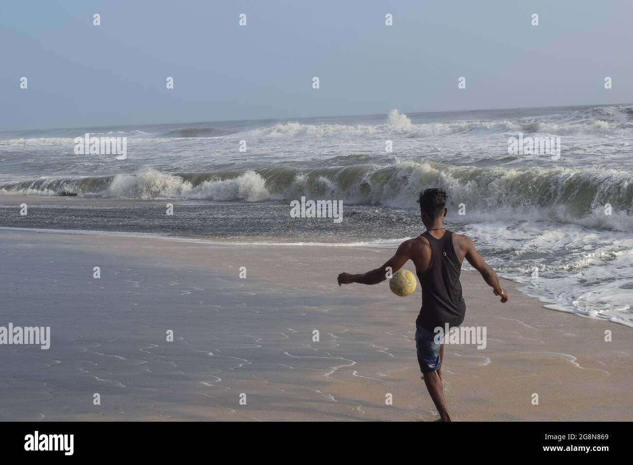 Homme jouant au football sur la plage seulement. Banque D'Images