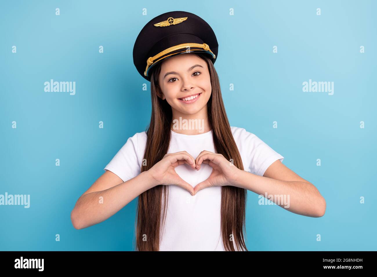 Portrait d'une jolie fille gaie portant un chapeau montrant le symbole du coeur isolé sur fond bleu vif Banque D'Images