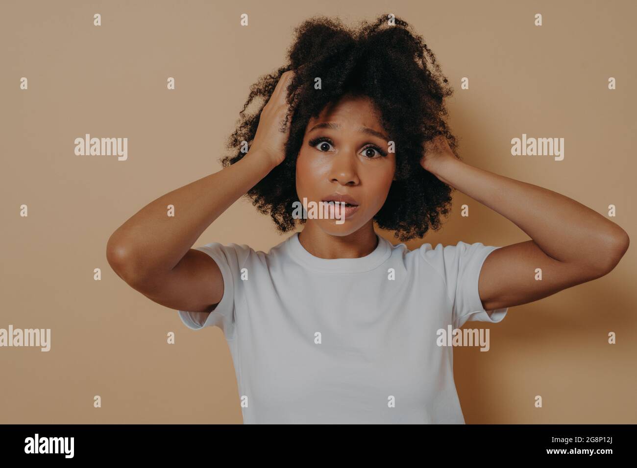 Femme africaine préoccupée et stressée avec une bouche ouverte tenant la tête dans les mains isolées sur fond beige Banque D'Images