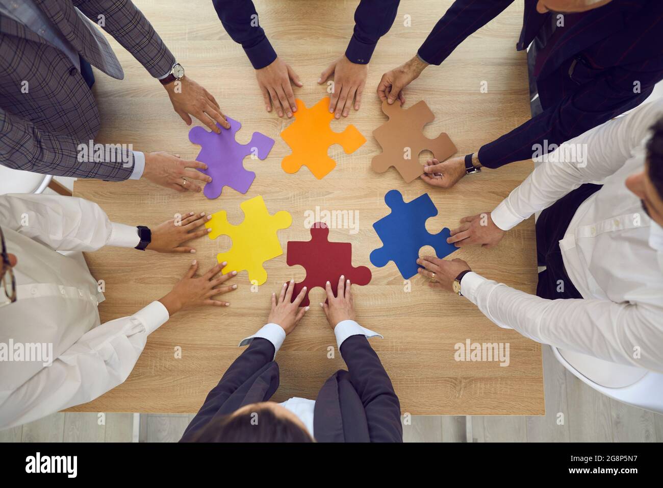 Équipe d'affaires se tenant autour d'une table de bureau essayant de faire correspondre des pièces d'un puzzle Banque D'Images