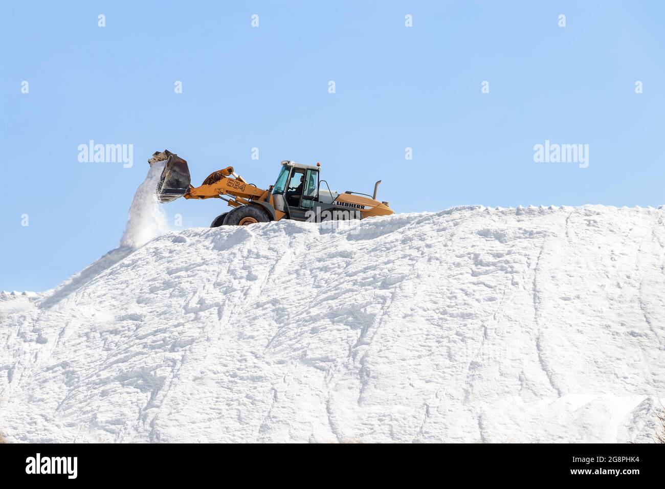 Huelva, Espagne - 1er octobre 2020 : pelle hydraulique travaillant dans une énorme pile de sel dans des salines. Sel marin produit par l'évaporation de l'eau de mer. Banque D'Images