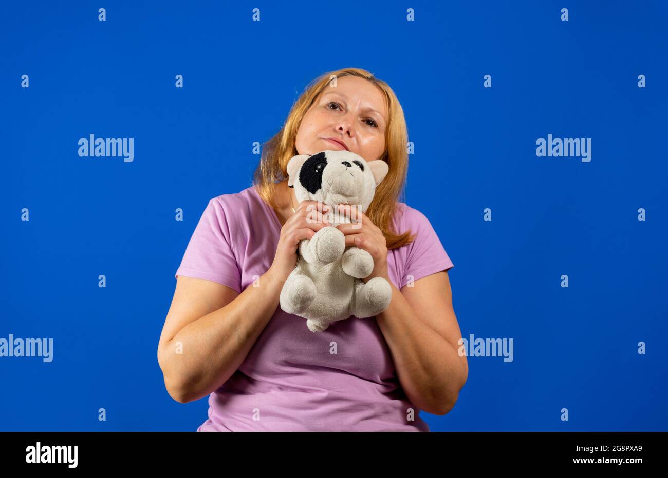 Jolie femme d'âge moyen jouant avec un chiot bourré sur fond bleu studio. Banque D'Images