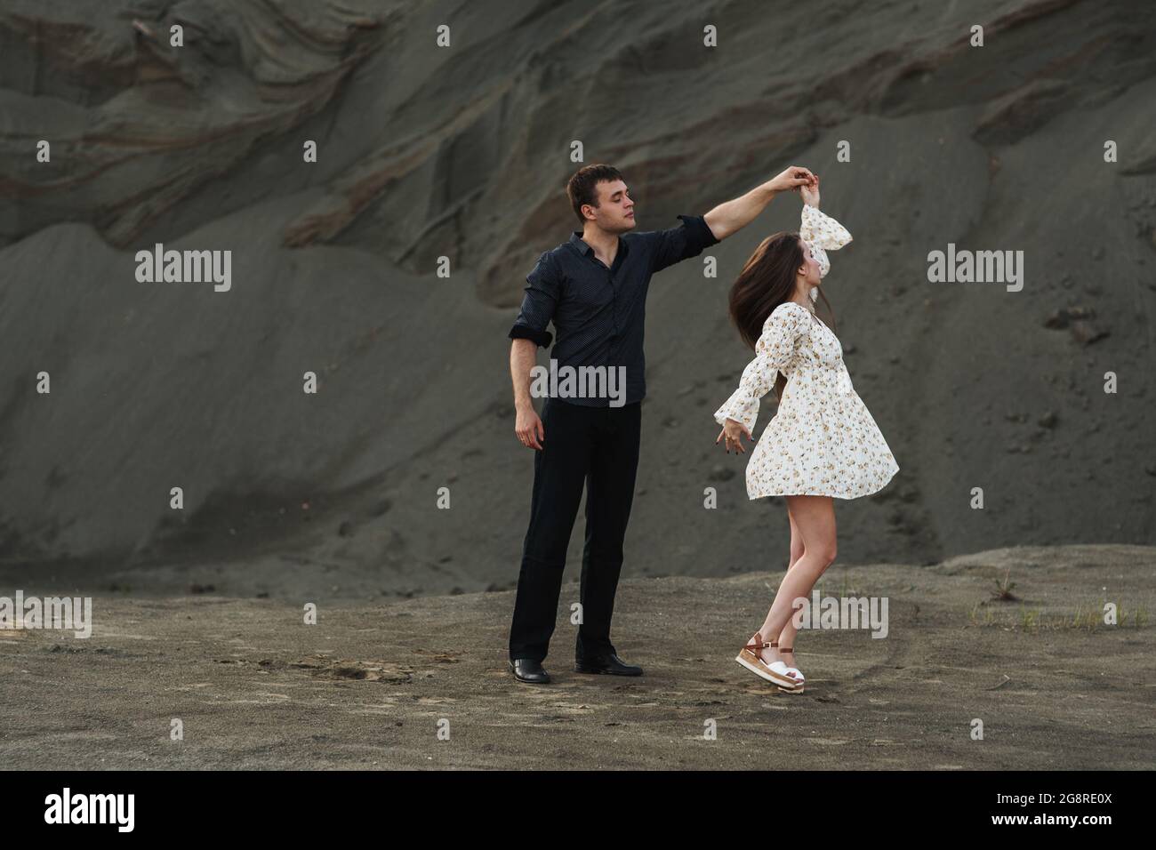 Couple heureux dansant et kissinc en plein air en été sur fond de sable gris Banque D'Images