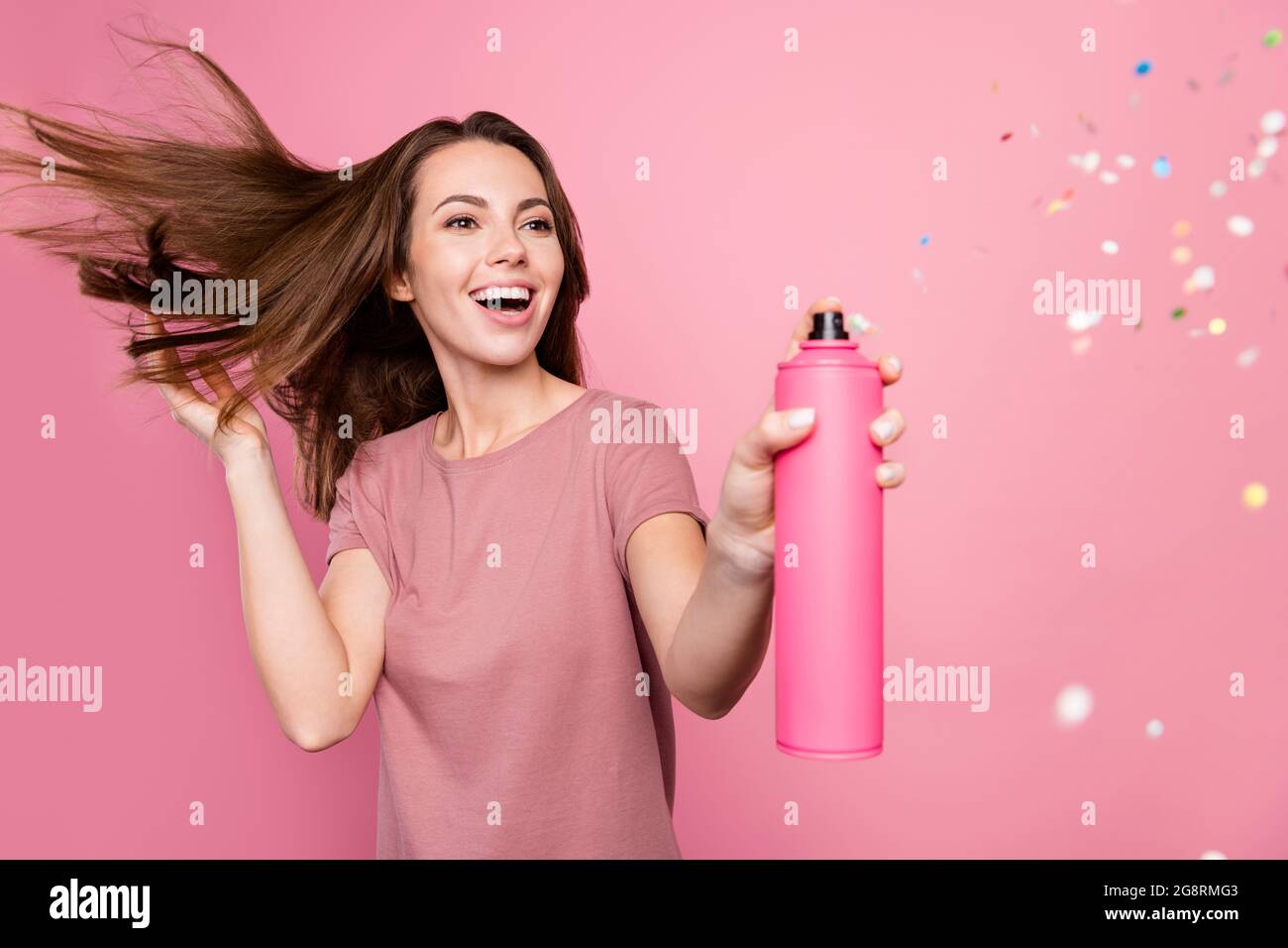 Photo de jolie excitée jeune femme porter ensemble décontracté sourire application pailletée cheveux spray isolé couleur rose fond Banque D'Images