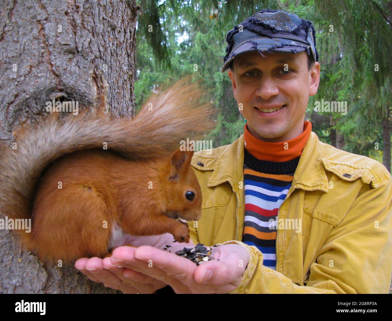 Un homme avec un écureuil dans ses bras se tient près d'un arbre. Le concept d'écologie et de protection de l'environnement. Banque D'Images