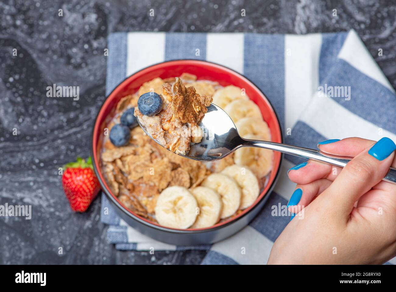 Muesli. Petit déjeuner, alimentation saine et alimentation. Muesli au lait et aux fruits dans une assiette sur un dessus en marbre noir. Main de femme avec une cuillère Banque D'Images