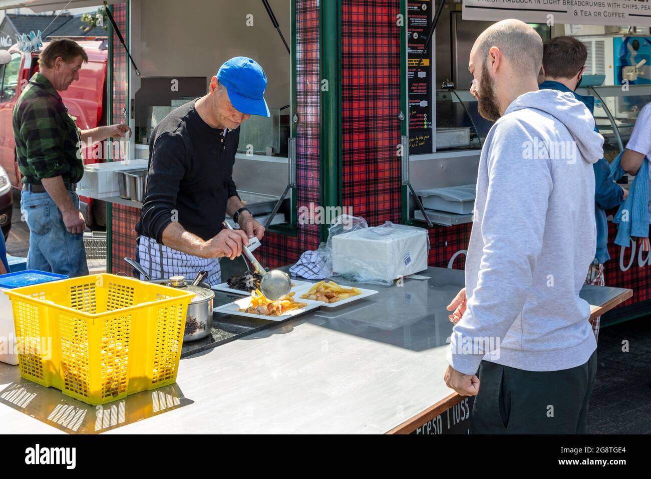 Une cabine de nourriture vendant des plats de poisson frais sur le port à Oban, Argyll, Écosse, Royaume-Uni avec un client masculin qui a récupéré sa commande. Banque D'Images