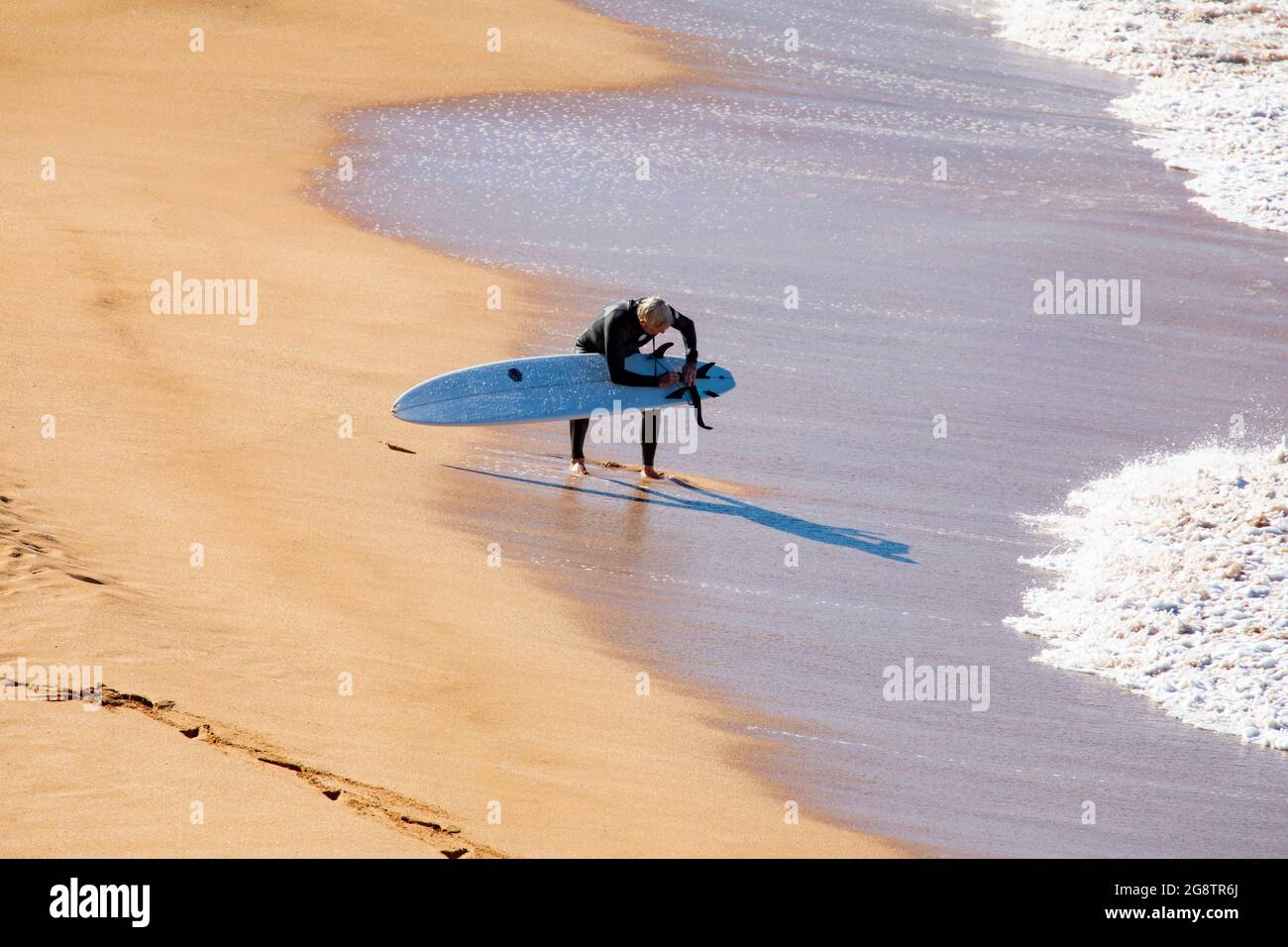 Un surfeur australien d'âge moyen sur une plage de Sydney ajuste sa planche de surf, Sydney, Australie Banque D'Images