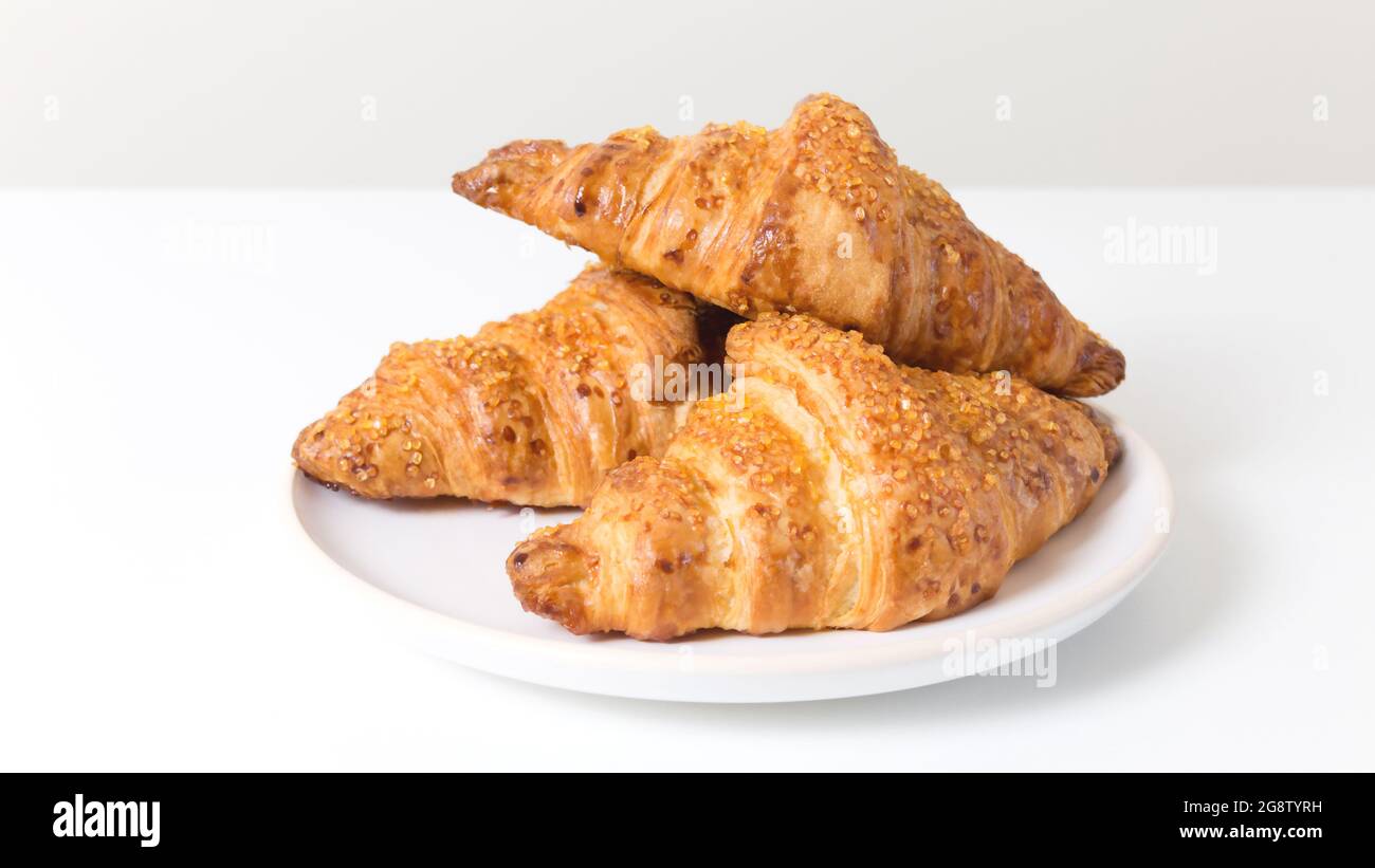 Assiette blanche avec trois croissants savoureux sur fond blanc. Cuisine française Banque D'Images