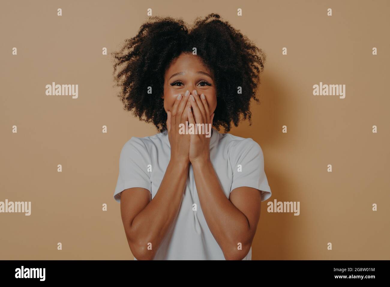Surprise femme excitée à la peau sombre en chemise blanche couvrant sa bouche avec les mains Banque D'Images
