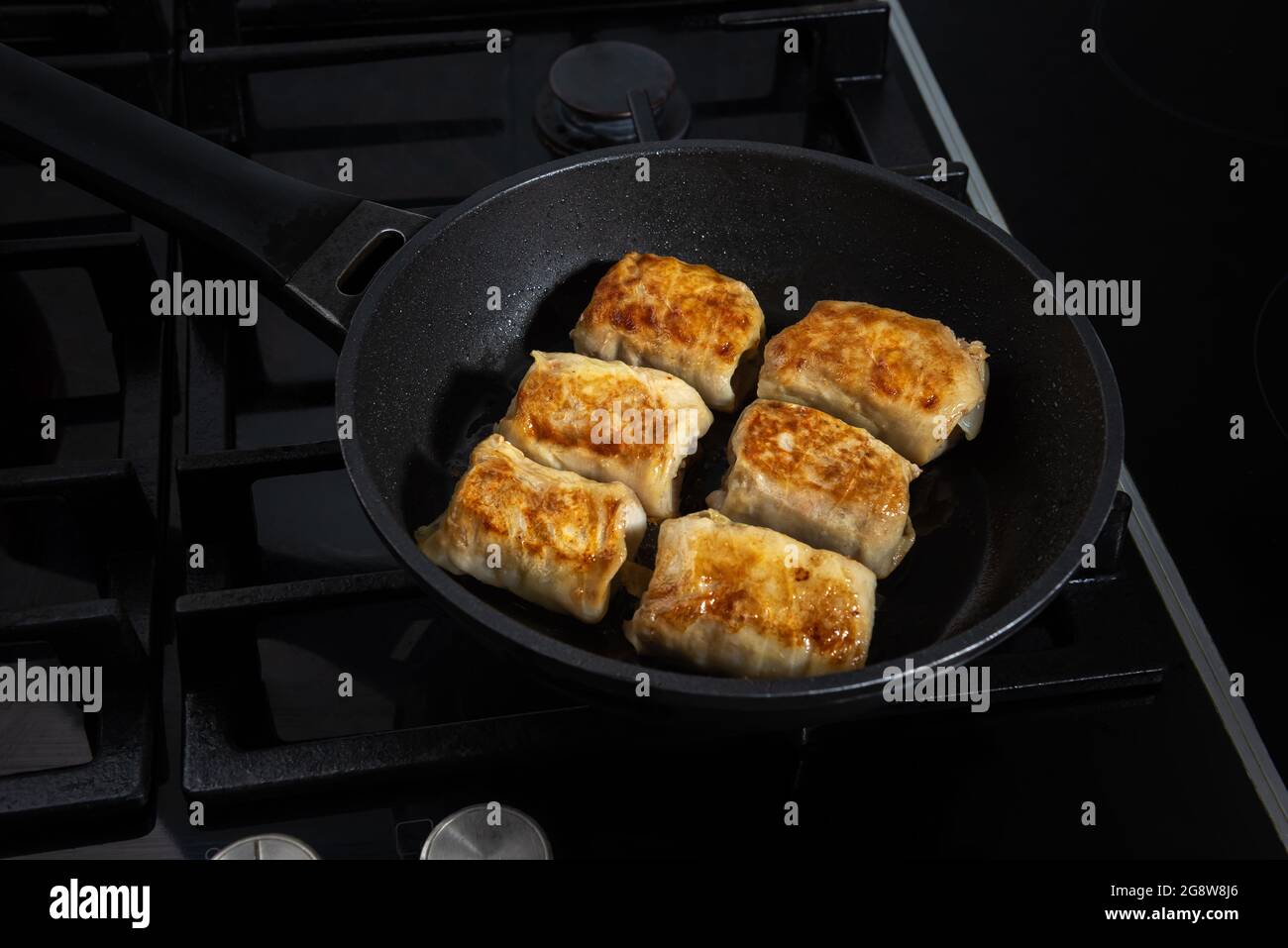 Processus de cuisson des petits pains de chou farcis faits maison. Peu de petits pains sont frits sur une poêle et sur une cuisinière noire. Les petits pains fraîchement frits sont couverts Banque D'Images