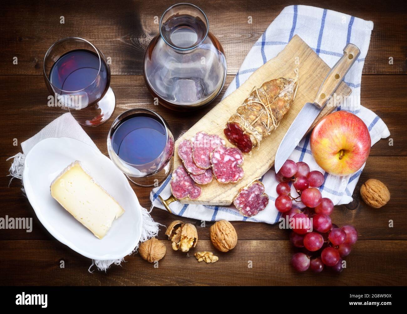 Salami, fromage, raisin, pomme, noix et vin rouge sur fond de bois, vue de dessus. Banque D'Images