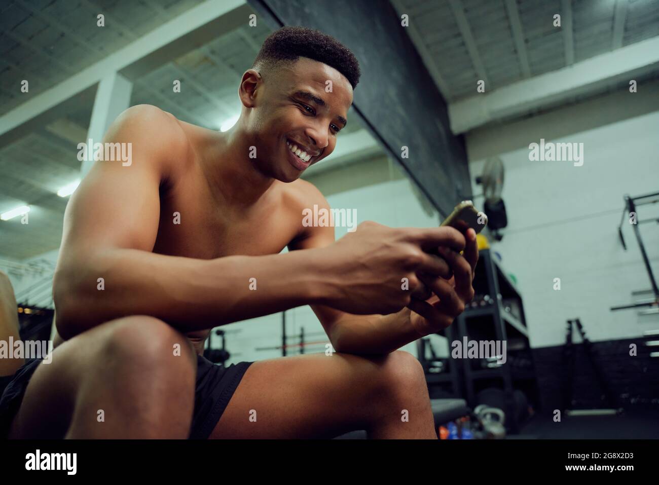 Jeune Afro-américain regardant son téléphone pour répondre à un message en ligne. Heureux, homme de course mixte souriant à son téléphone tout en s'asseyant dans le Banque D'Images