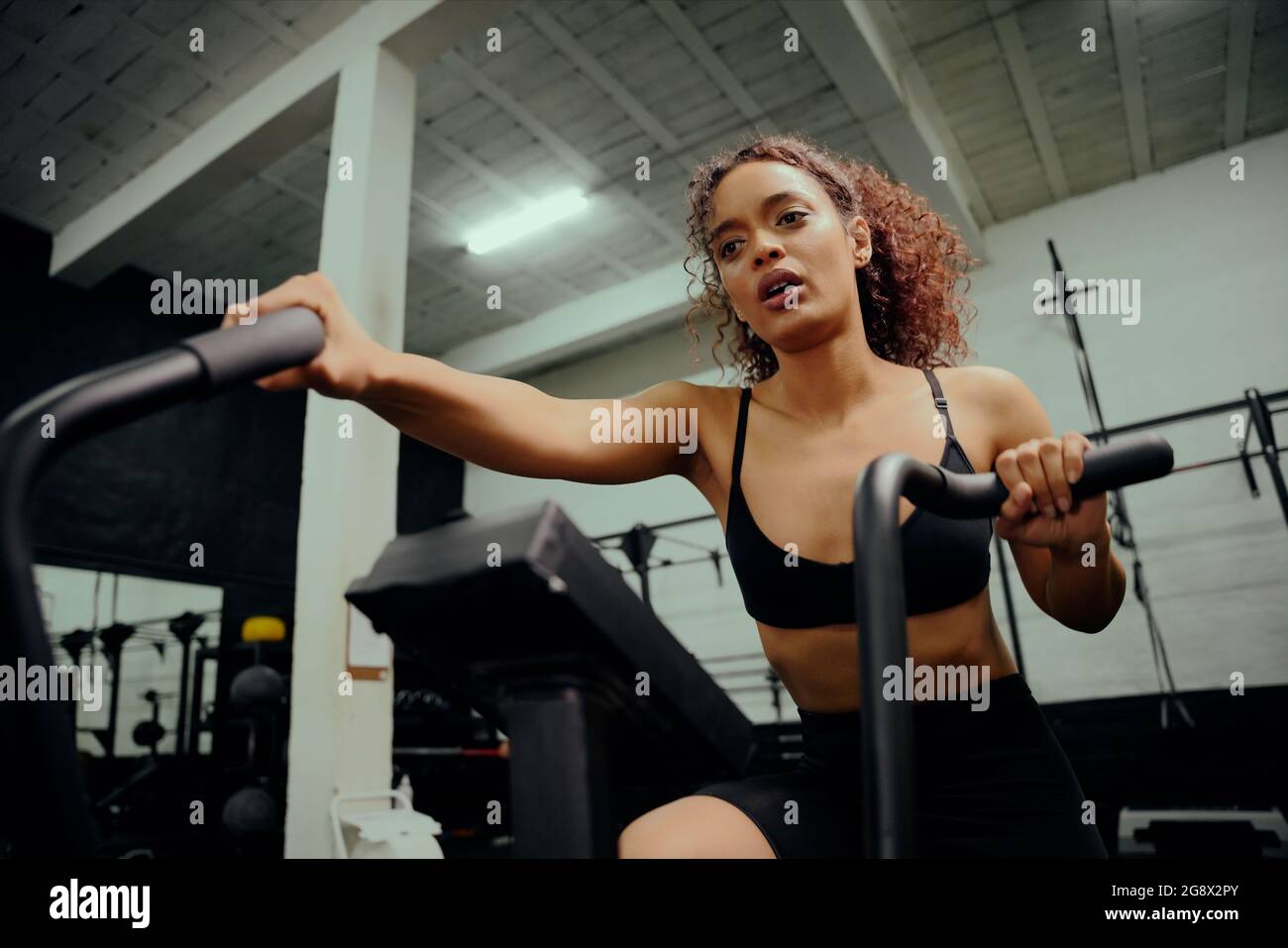 Femme afro-américaine utilisant une machine elliptique pendant l'entraînement multidisciplinaire. Une athlète féminine s'entraîner dans la salle de sport. Photo de haute qualité Banque D'Images