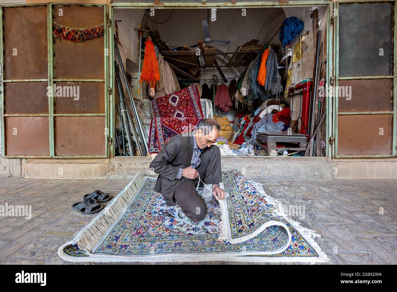 L'homme local arrange les franges du tapis persan dans le bazar à Yazd, en Iran Banque D'Images