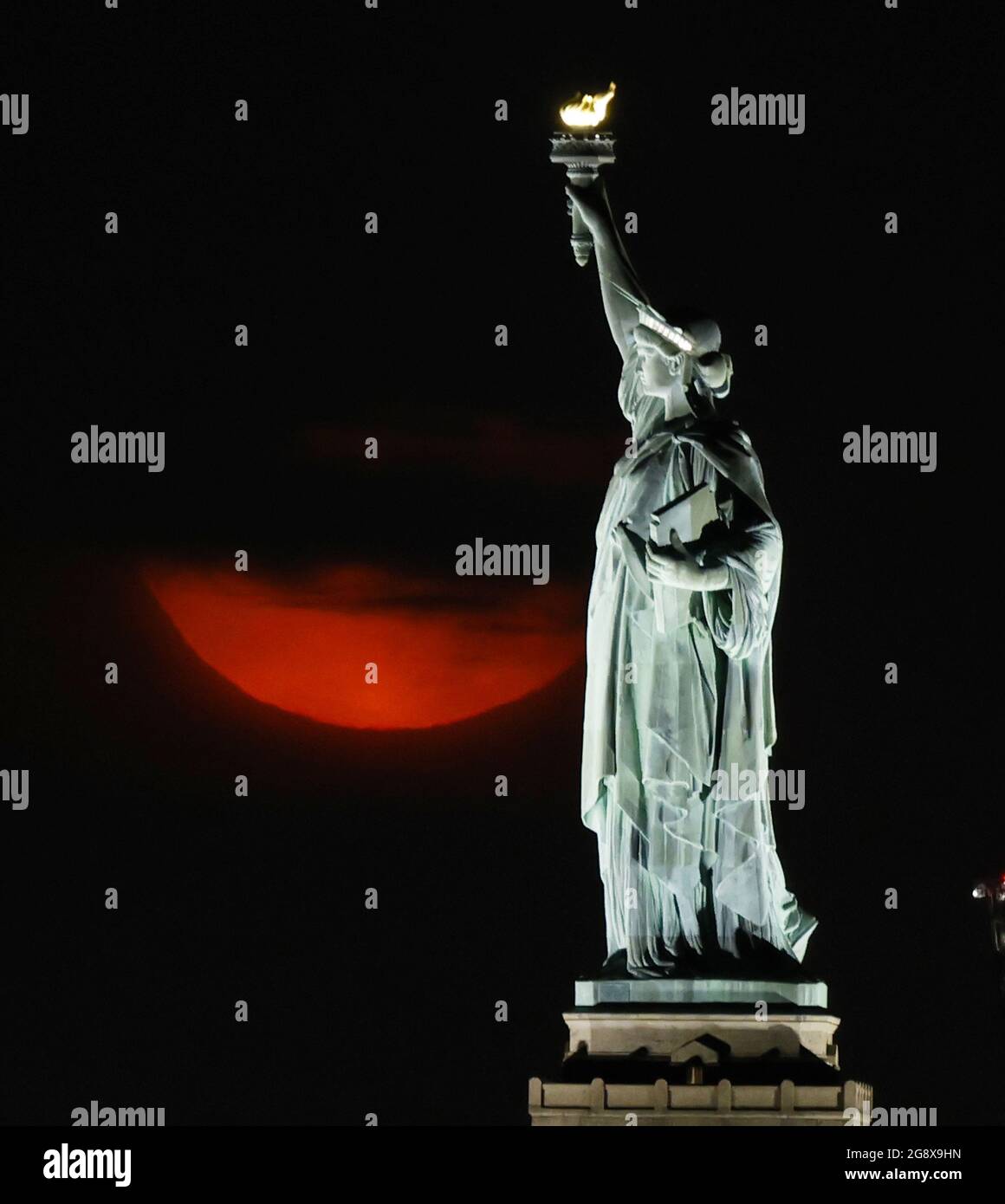 New York, États-Unis. 23 juillet 2021. Une pleine Buck Moon, partiellement obstruée par des nuages, se pose derrière la Statue de la liberté à New York le vendredi 23 juillet 2021. Photo de John Angelillo/UPI crédit: UPI/Alay Live News Banque D'Images