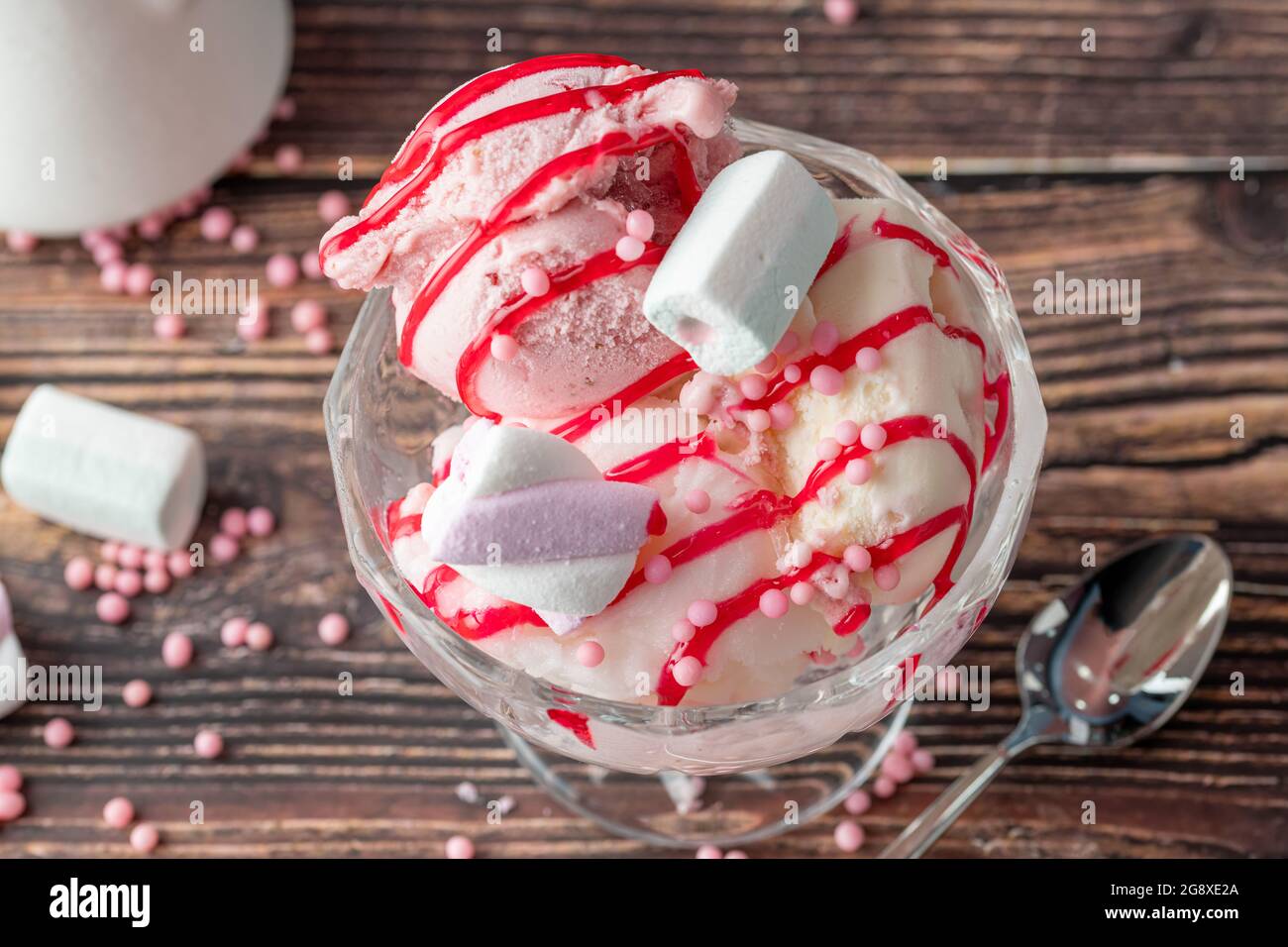 Crème glacée Roma à la fraise, à la banane et à la crème dans un bol en verre avec sauce rouge versée dessus. Banque D'Images