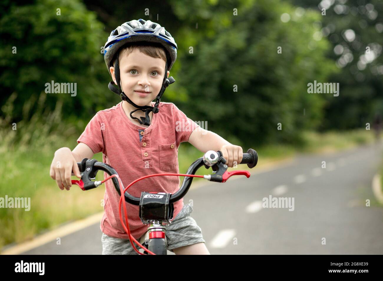 Enfant à vélo sur la piste cyclable sous la pluie. Enfant en casque  apprenant à monter l'été. Joyeux garçon à vélo, s'amuser en plein air dans  la nature. Actif Photo Stock -