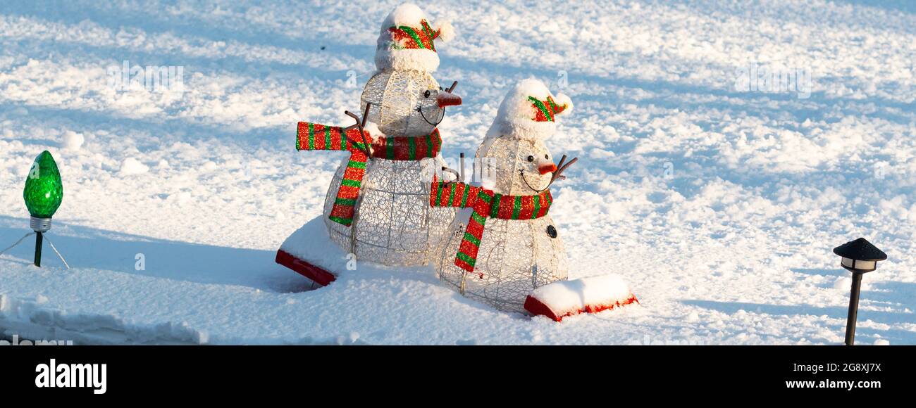 Deux bonhommes de neige sur un traîneau dans la décoration de neige sur une pelouse devant. Banque D'Images