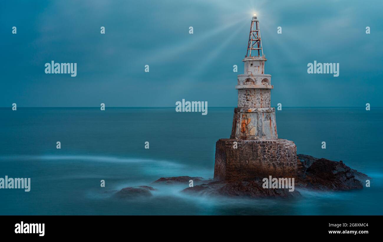 Ancienne tour de phare blanche isolée dans l'eau de mer bleu calme après le coucher du soleil près d'Ahtopol sur la côte de la mer Noire, Bulgarie. Paysage de phare émettant li Banque D'Images