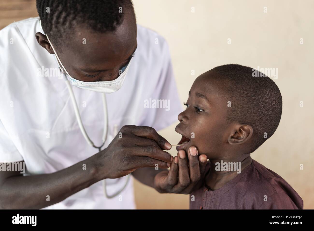 Dans cette image, un petit garçon africain courageux collabore avec son infirmière noire lors d'un examen par écouvillon buccal pour détecter le virus corona Banque D'Images