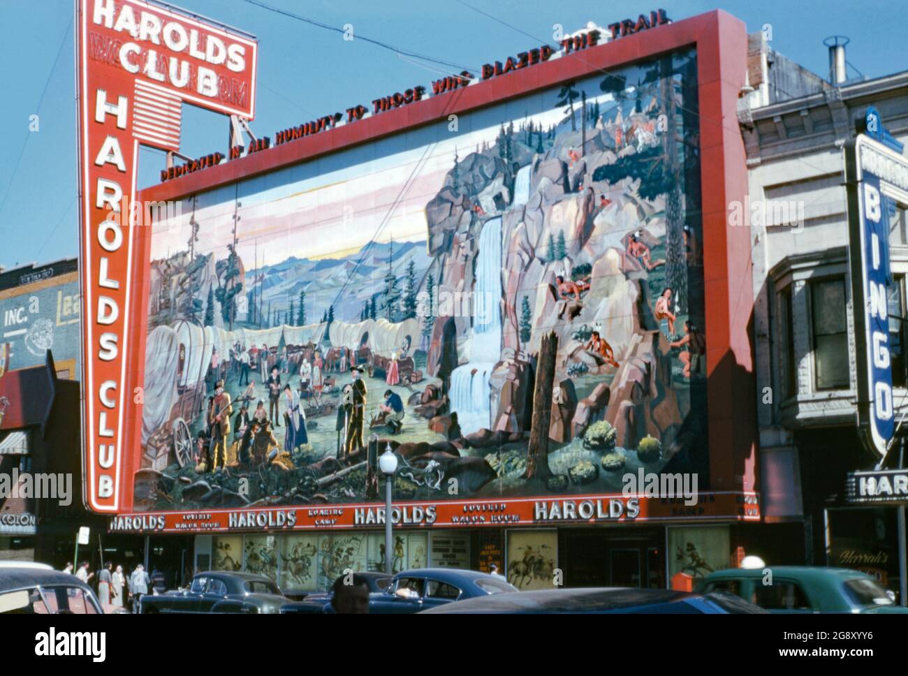 Harold's Club, un casino dans North Virginia Street, Reno, Nevada, États-Unis vu au milieu des années 1950. Le club a été créé en 1935. Une grande fresque de 70 mètres sur 35 pieds de colons pionniers de l'Ouest présentant un train à wagons et des Amérindiens a été exposée devant le casino. La fresque a été conçue en 1949 par Theodore McFallon et ses carreaux de céramique émaillés à la main ont été fabriqués par Sargent Claude Johnson. Au-dessus de la fresque, il a déclaré «mort en toute humilité à ceux qui ont fait le chemin». Le bâtiment a été démoli en 1999. La fresque a été exposée en 2007 au Reno Livestock Events Center. Banque D'Images