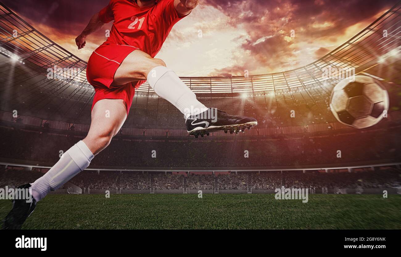 Gros plan d'une scène de football pendant un match avec un joueur dans un uniforme rouge donnant le coup de pied au ballon avec la puissance Banque D'Images