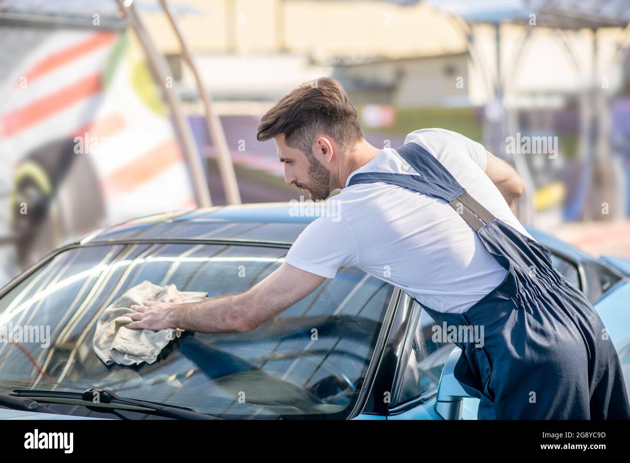 Homme dans une chemise et une combinaison essuyant le verre propre de la voiture Banque D'Images