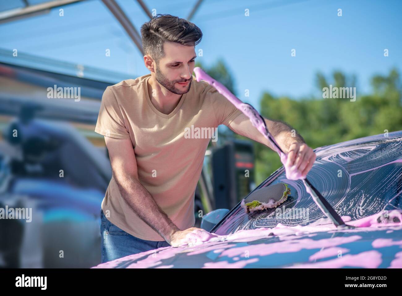 Jeune barbu souriant homme qui lave l'essuie-glace de pare-brise Banque D'Images Jeune barbu souriant homme qui lave l'essuie-glace de pare-brise Banque D'Images