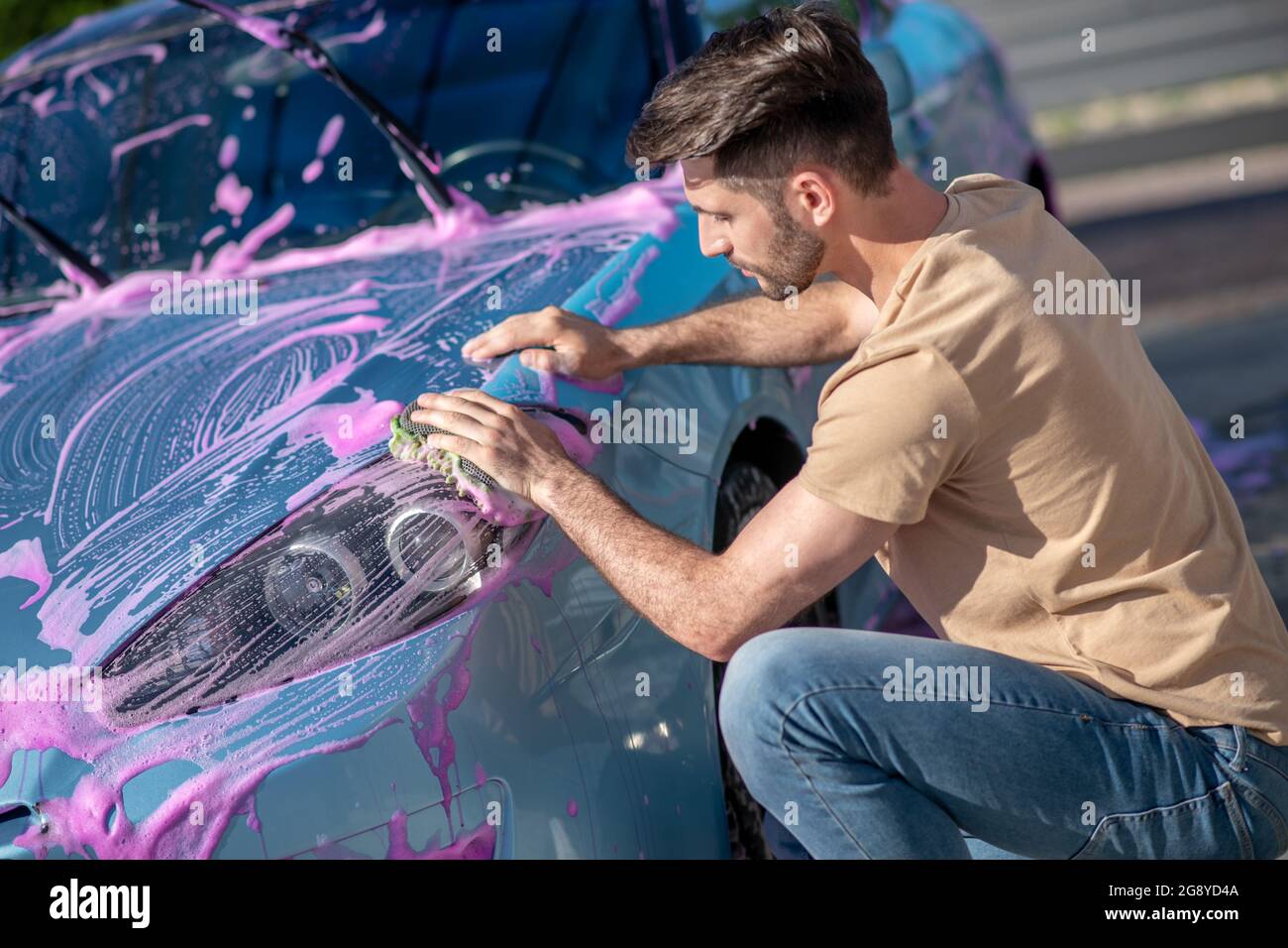 Un homme attentif lave la voiture avec de la mousse rose Banque D'Images