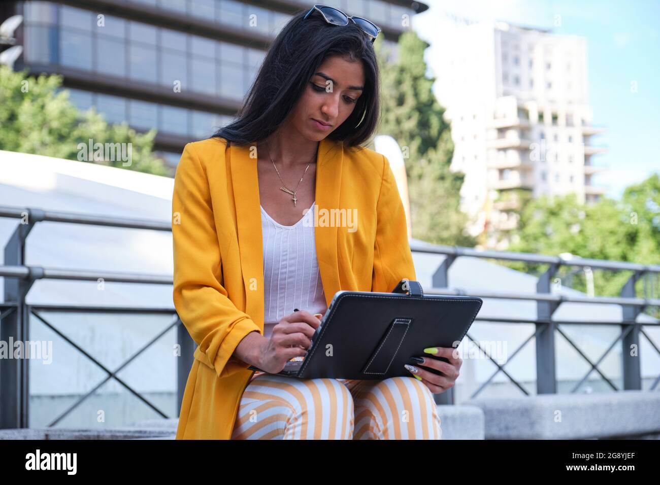 Jeune femme d'affaires latine portant une veste de costume jaune  travaillant avec une tablette assise à l'extérieur Photo Stock - Alamy