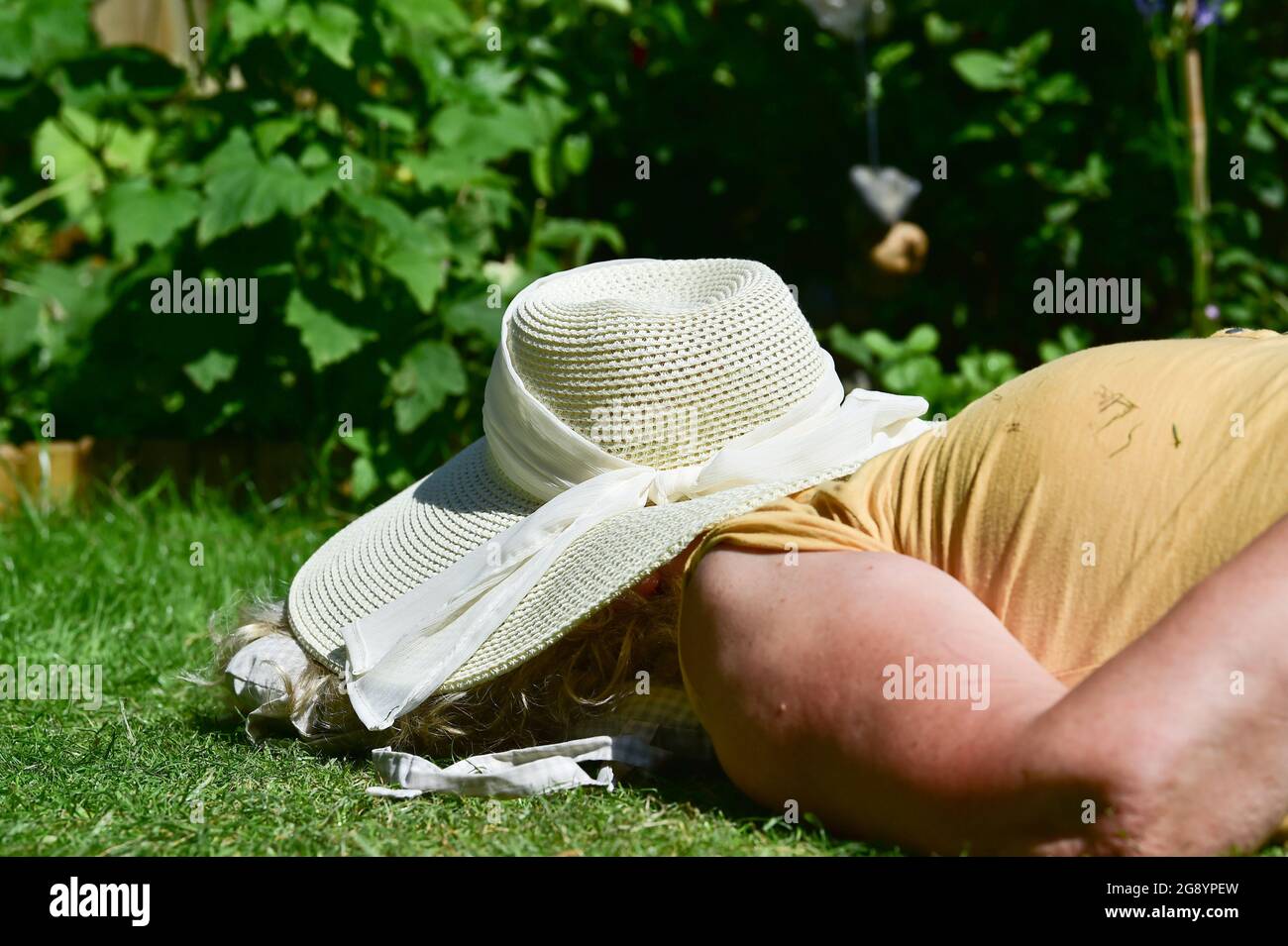 Femme posée sur le dos sur l'herbe avec un chapeau de soleil sur son visage dans le jardin été Royaume-Uni Banque D'Images