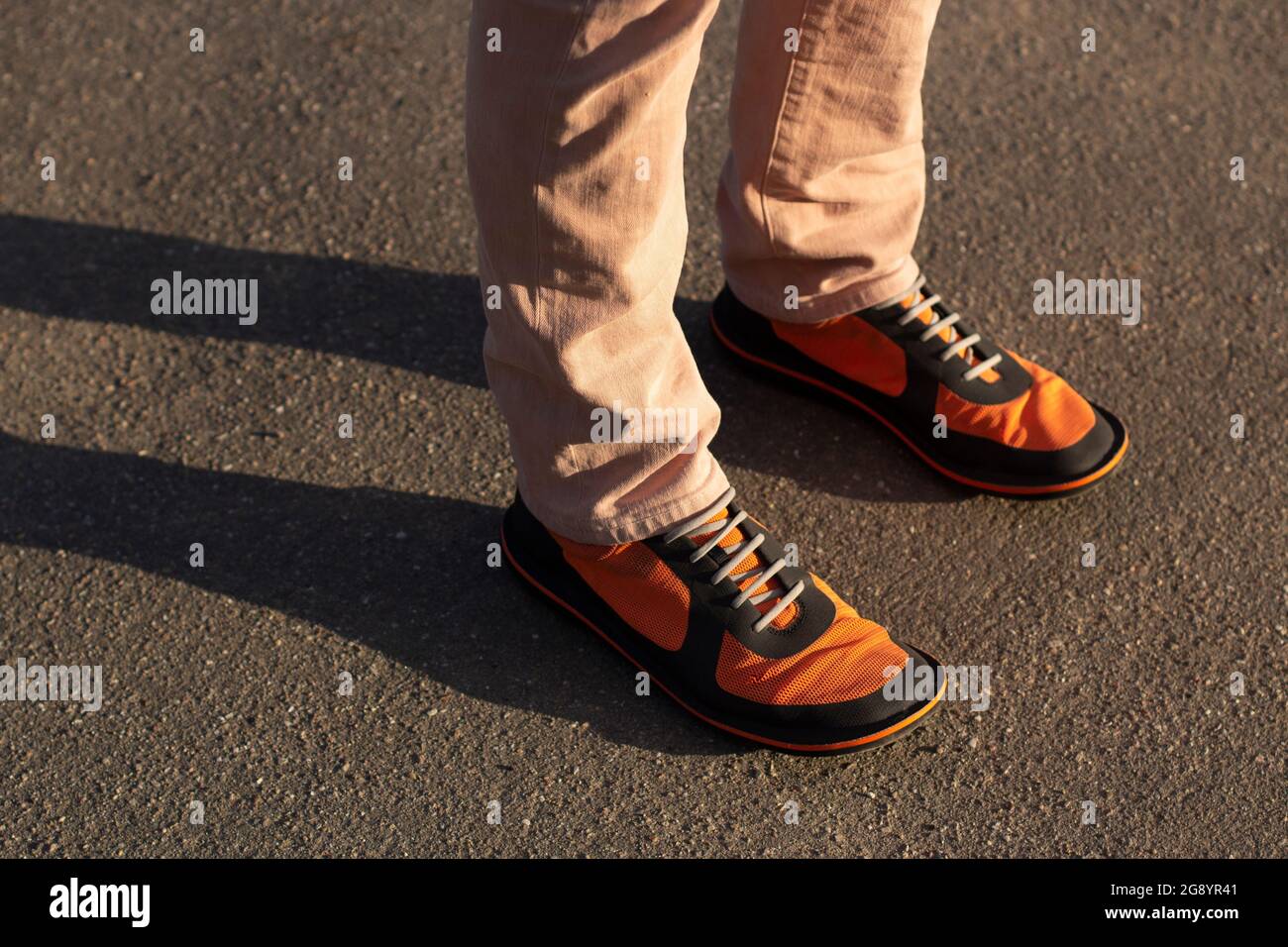 Des bottes orange sur leurs pieds. Chaussures tendance au soleil. Un homme en baskets dans la rue. Des vêtements brillants pour les pieds. Un homme avec une grande taille de jambe Banque D'Images