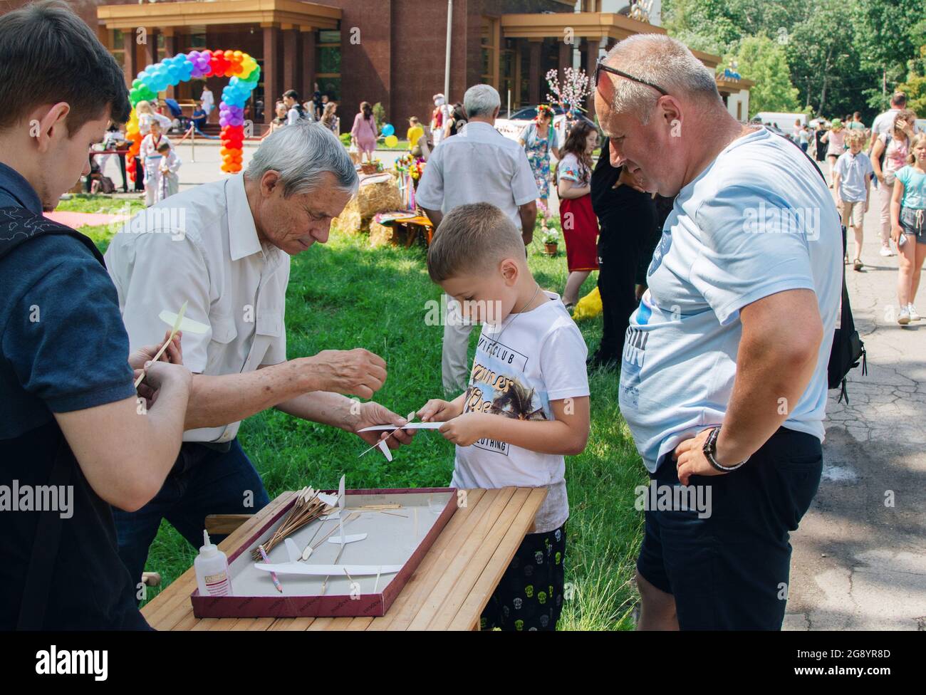 Zaporizhia, Ukraine- 19 juin 2021: Festival de la famille de charité: Un homme volontaire enseignant des garçons à faire des avions de carton jouet à l'atelier de modélisation en plein air Banque D'Images
