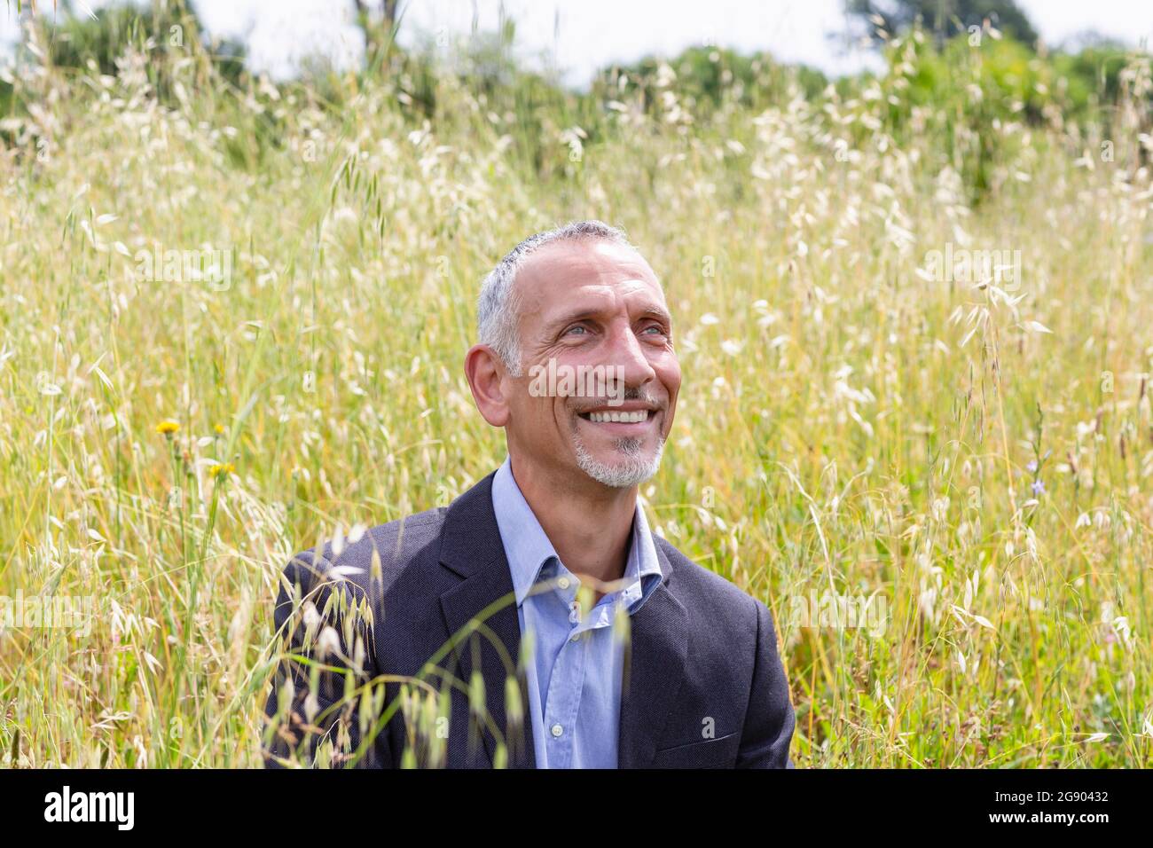 Professionnel souriant, homme d'affaires, qui regarde loin tout en étant assis dans un champ herbacé Banque D'Images