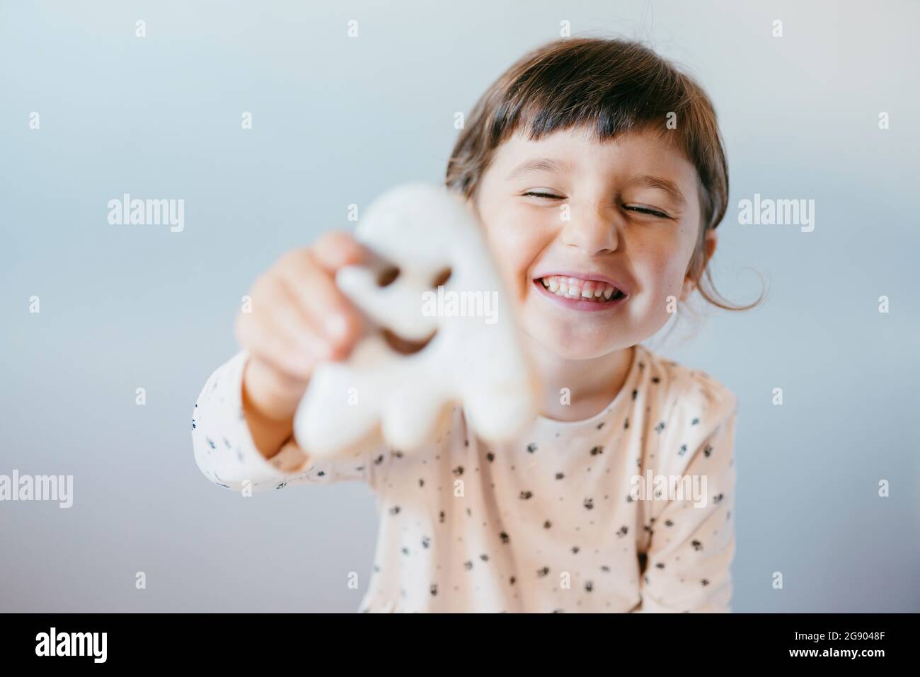 Petite fille gaie avec les yeux fermés montrant des biscuits fantômes Banque D'Images