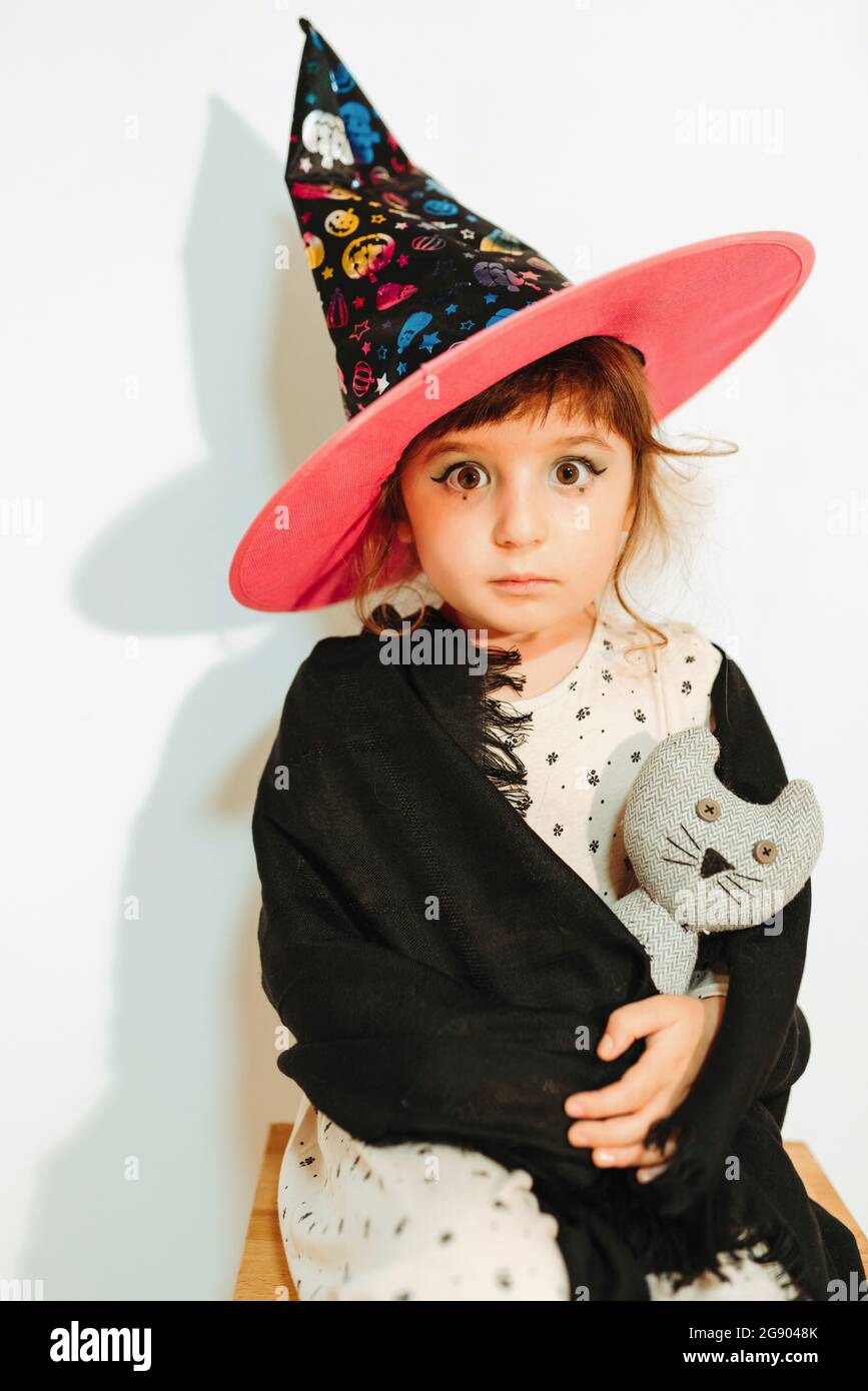 Fille habillée comme sorcière d'Halloween tenant le jouet bourré par le mur Banque D'Images