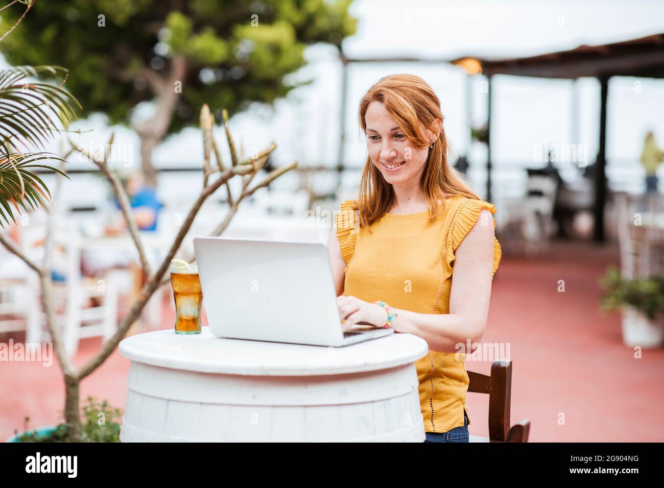 Femme souriante travaillant sur un ordinateur portable tout en étant assise au bar Banque D'Images
