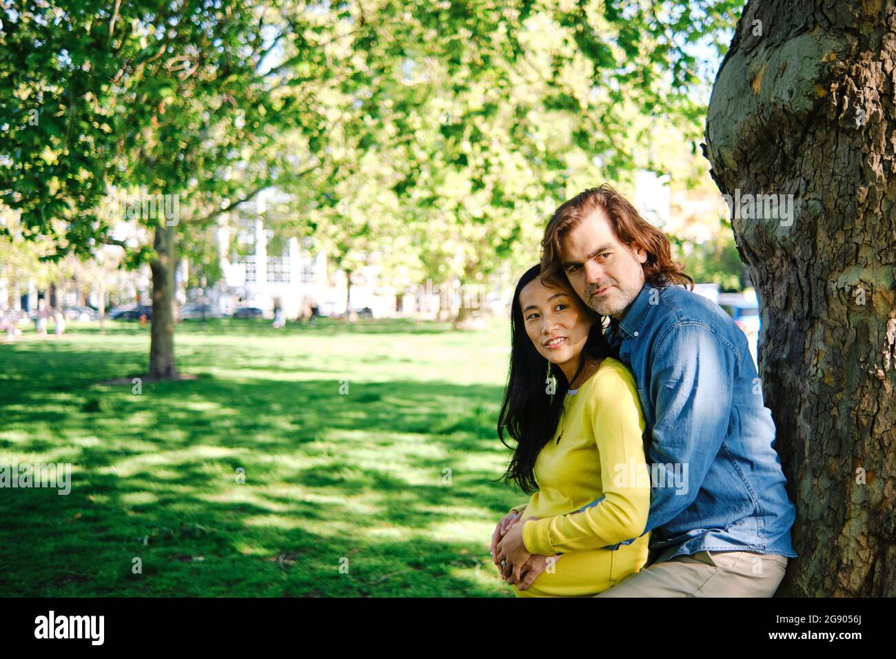 Homme s'appuyant sur l'arbre tout en embrassant femme enceinte dans le parc public Banque D'Images