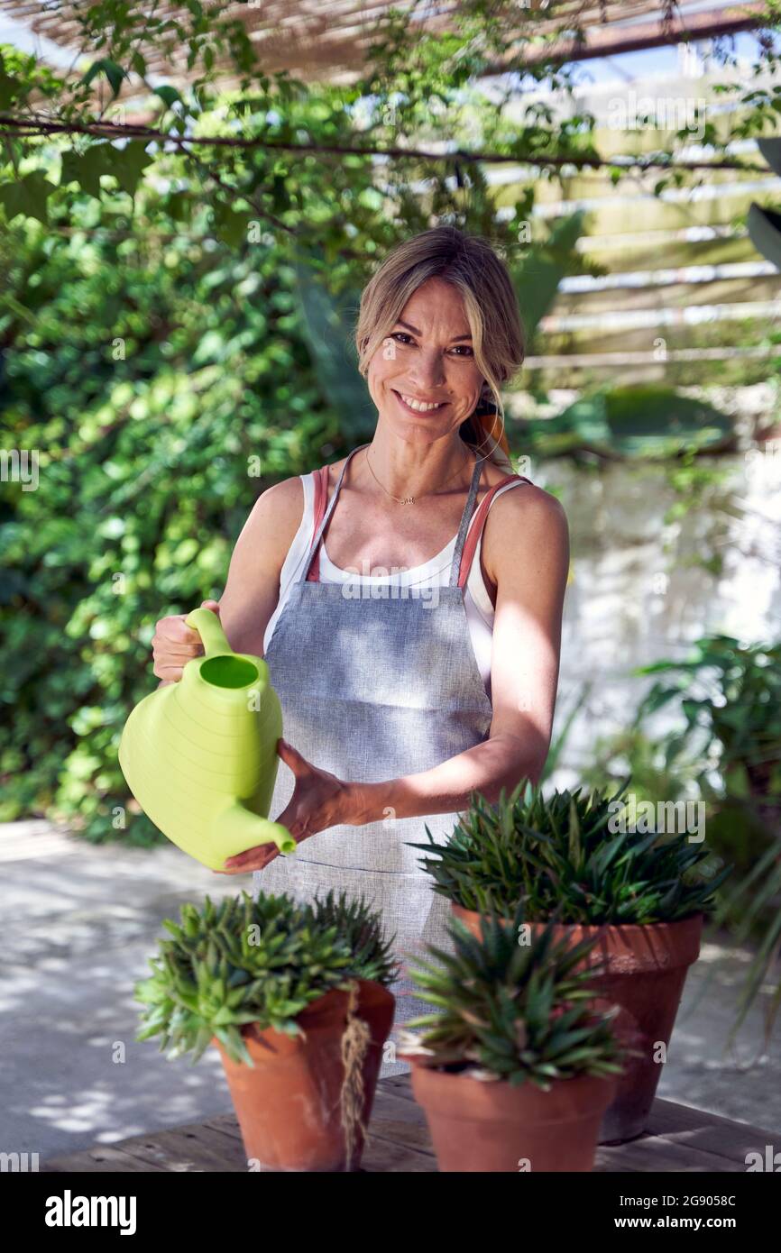 Femme mûre souriante arrosant les plantes tout en se tenant dans le jardin Banque D'Images