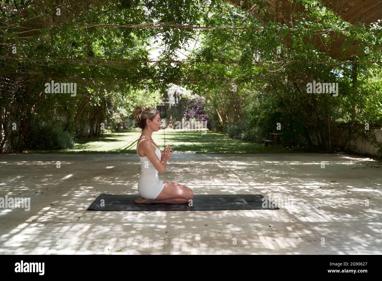 Femme à la main clasdée méditant sur le tapis d'exercice dans le jardin Banque D'Images
