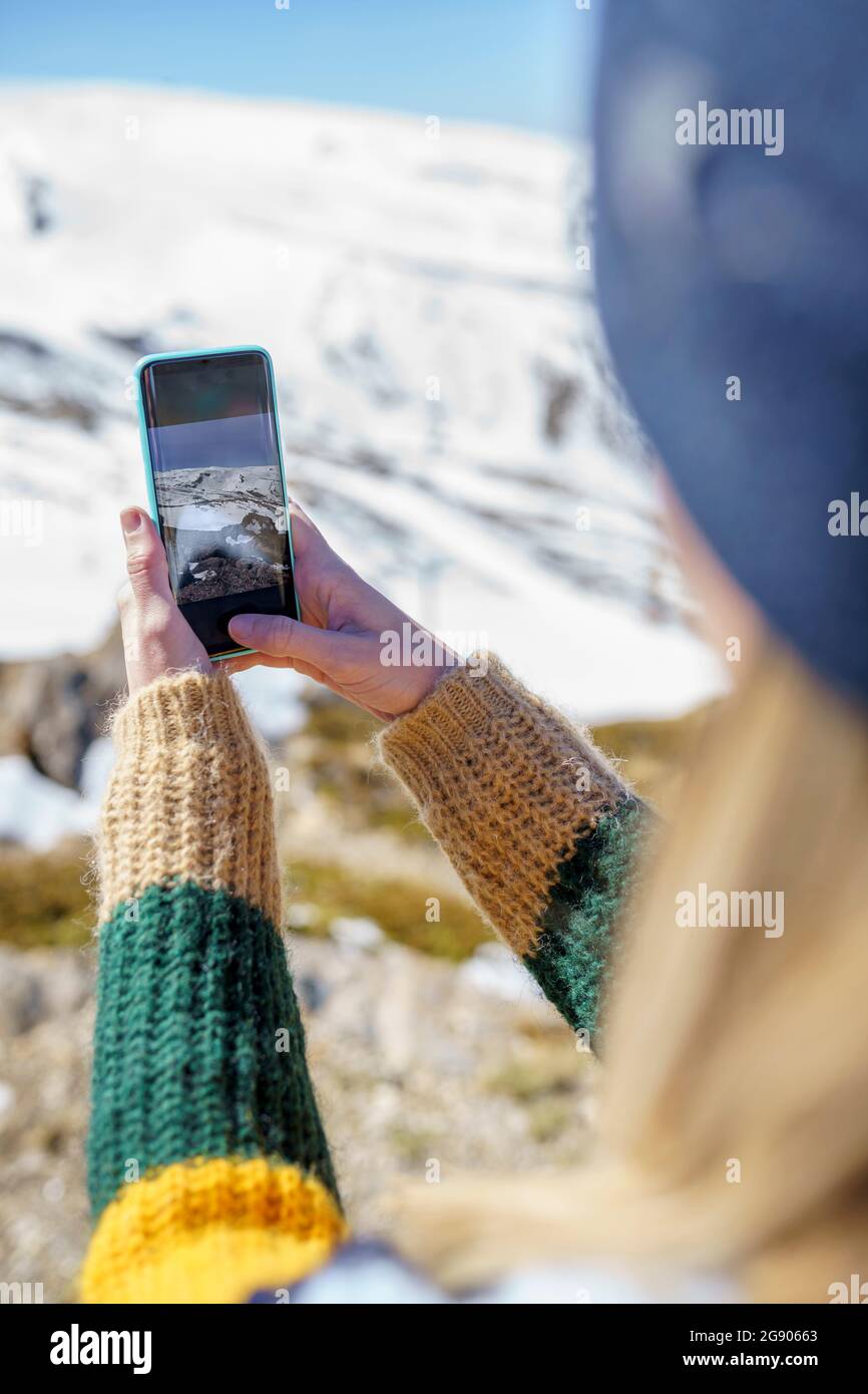 Femme photographiant une montagne enneigée à travers un téléphone portable pendant l'hiver Banque D'Images
