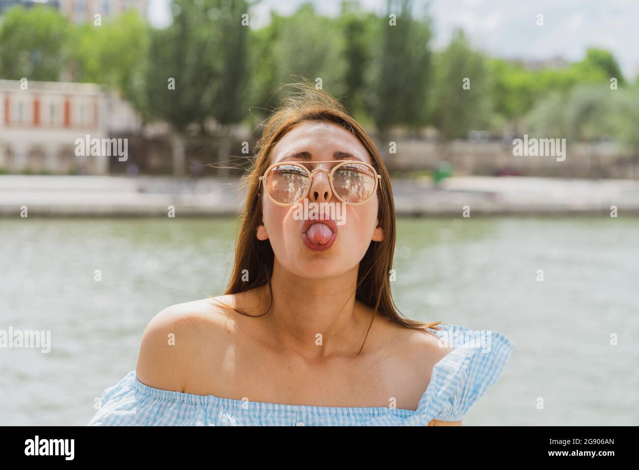Femme portant des lunettes de soleil qui collent la langue devant la rivière Banque D'Images