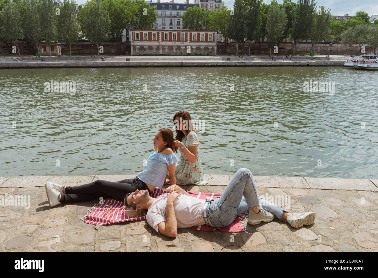 Femme nouant les cheveux de l'amie féminine par homme gay relaxant pendant la journée ensoleillée Banque D'Images