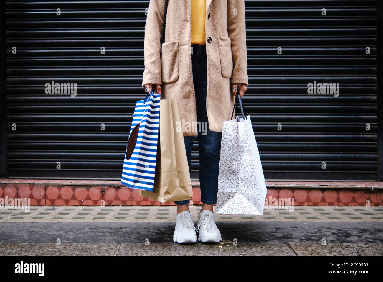 Femme tenant des sacs de shopping devant le volet fermé Banque D'Images