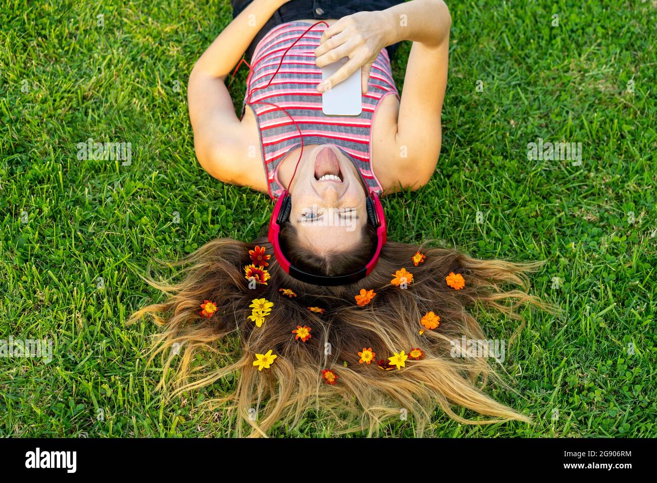 Jeune femme espiègle avec des fleurs dans les cheveux qui collent la langue sur l'herbe Banque D'Images
