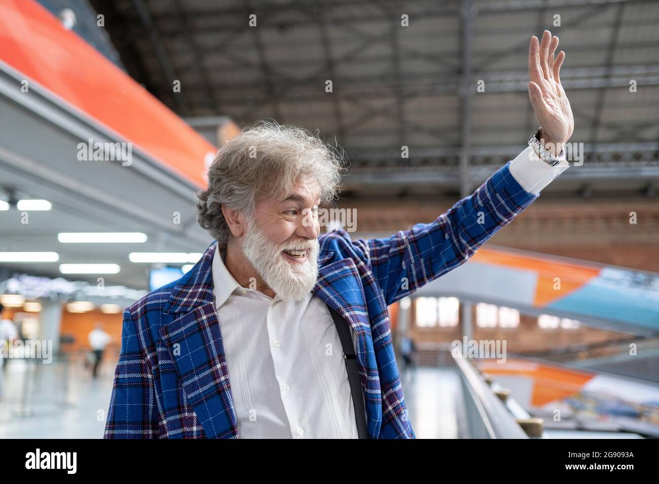 Homme mature à barbe blanche agitant la main en se tenant à la gare Banque D'Images