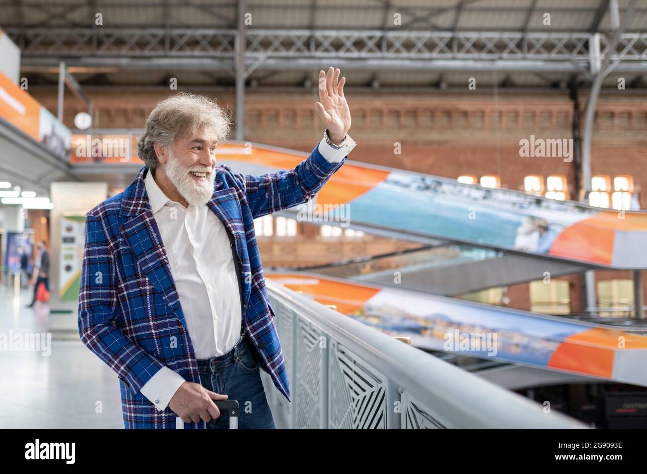 Homme mûr agitant la main tout en se tenant près de la main courante à la gare Banque D'Images