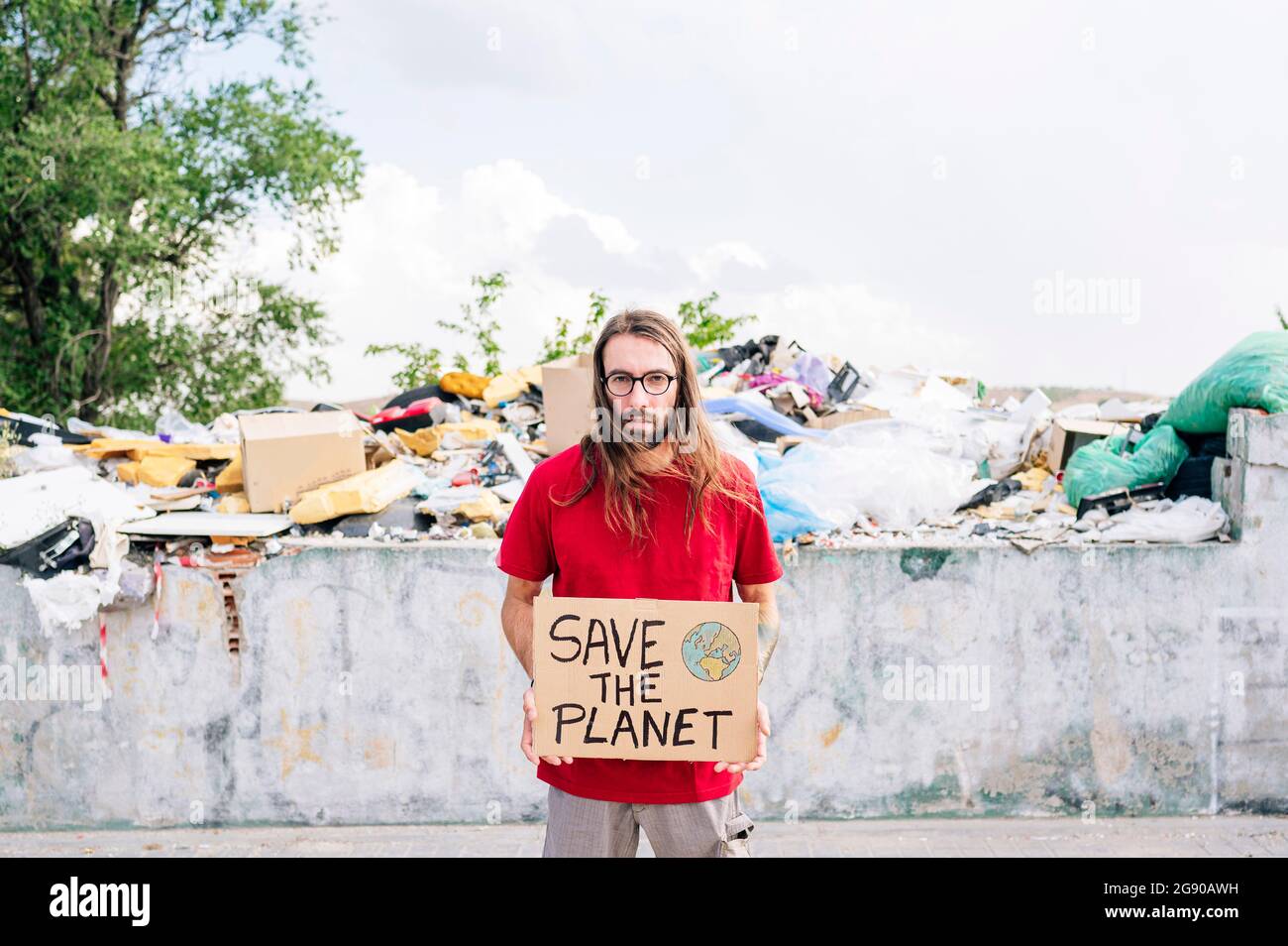 Hippie homme tenant le carton avec sauver la planète en face de près de décharge de déchets Banque D'Images